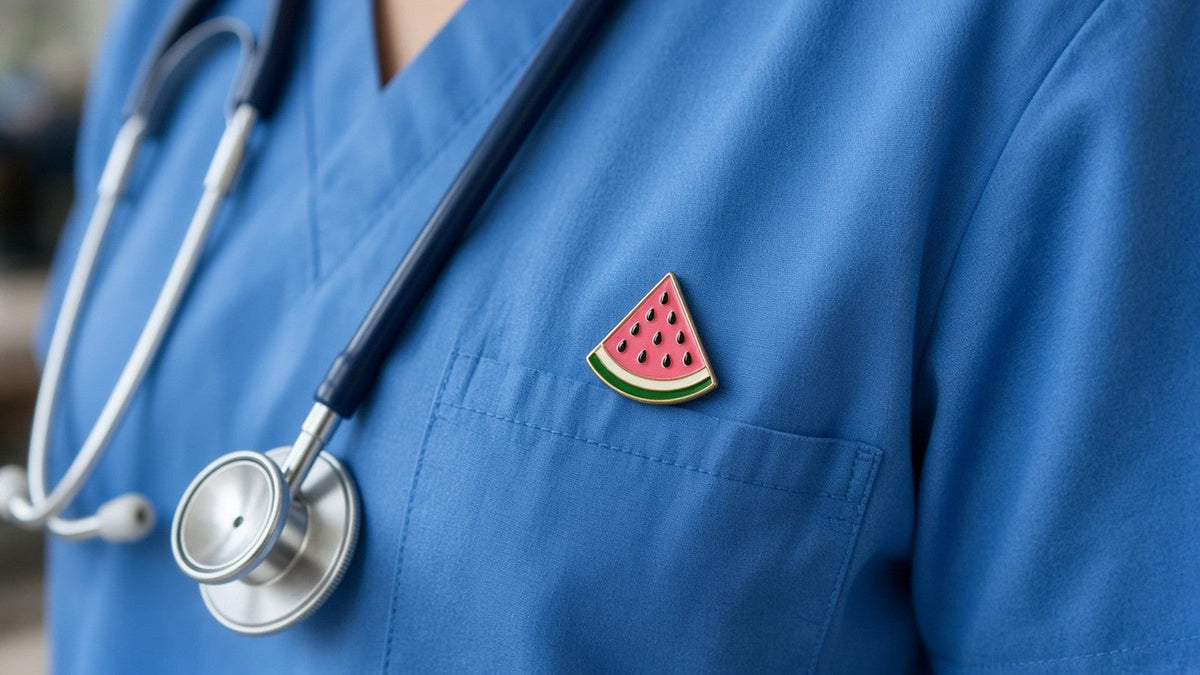 A small watermelon pin badge on the chest pocket of blue medical scrubs, with a stethoscope